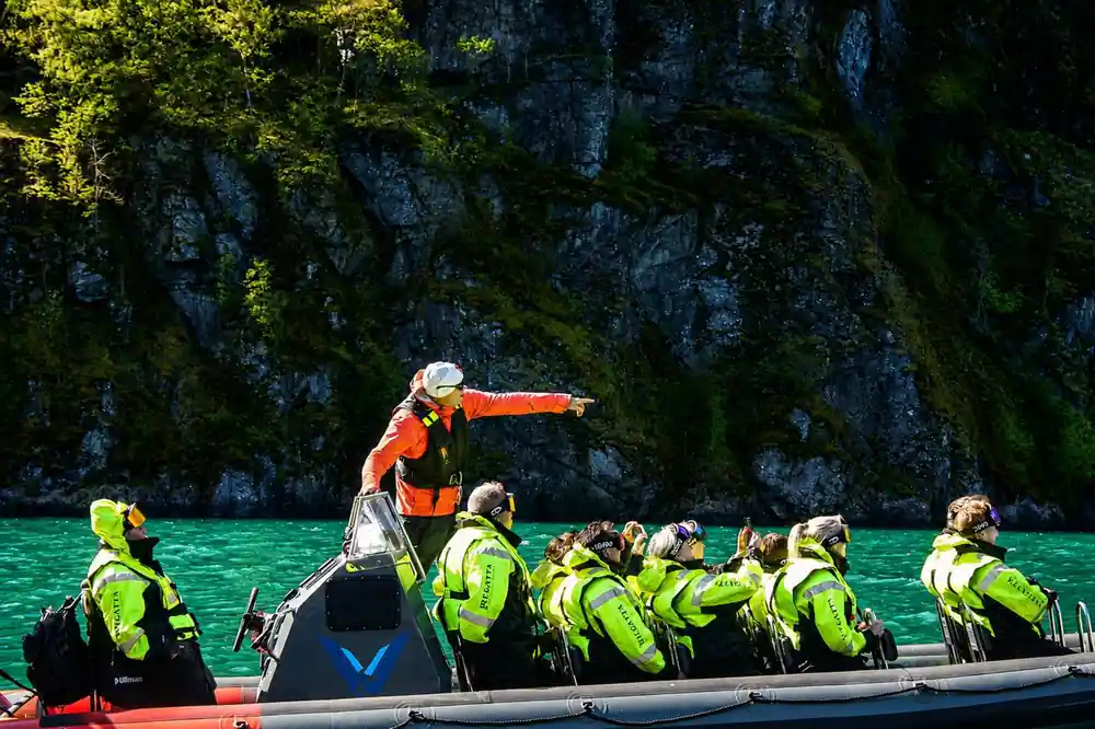 A guide standing and pointing out across the fjord to seated passengers