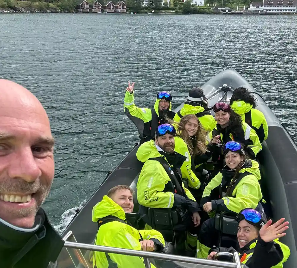 Passengers in survival suits and goggles waving from the boat