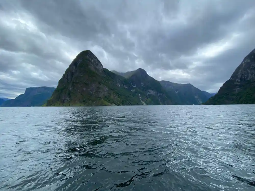 A pointed green summit under heavy cloud above flat water