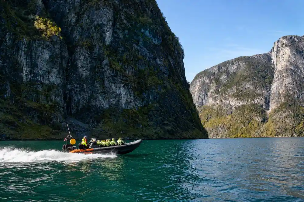 A small RIB dwarfed by the green walls of the fjord