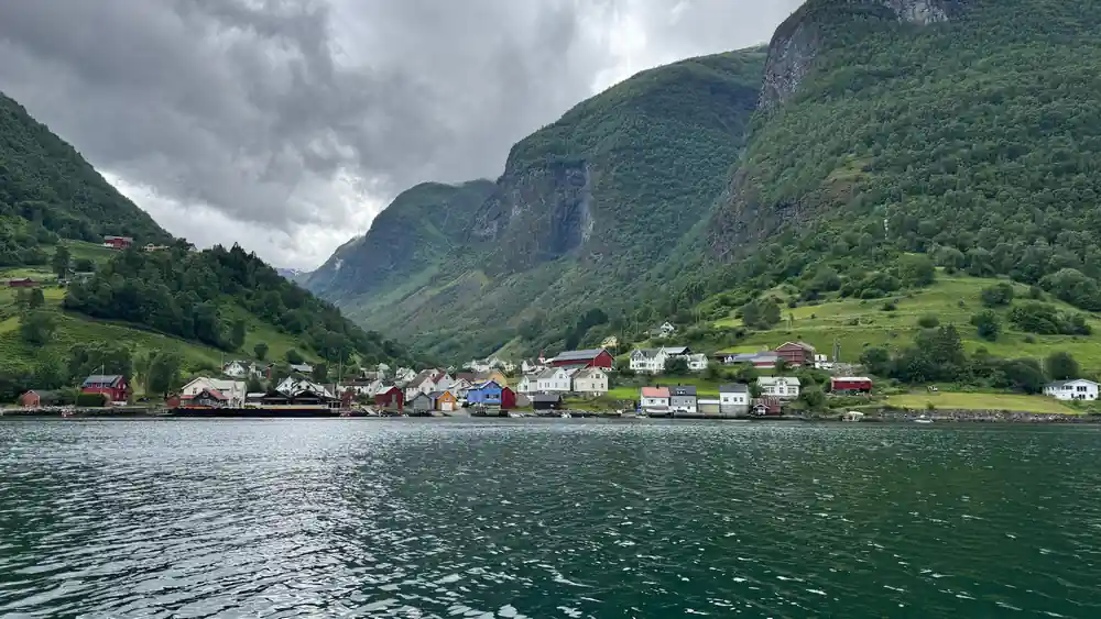 A village of white and red houses along the shore under a green mountain