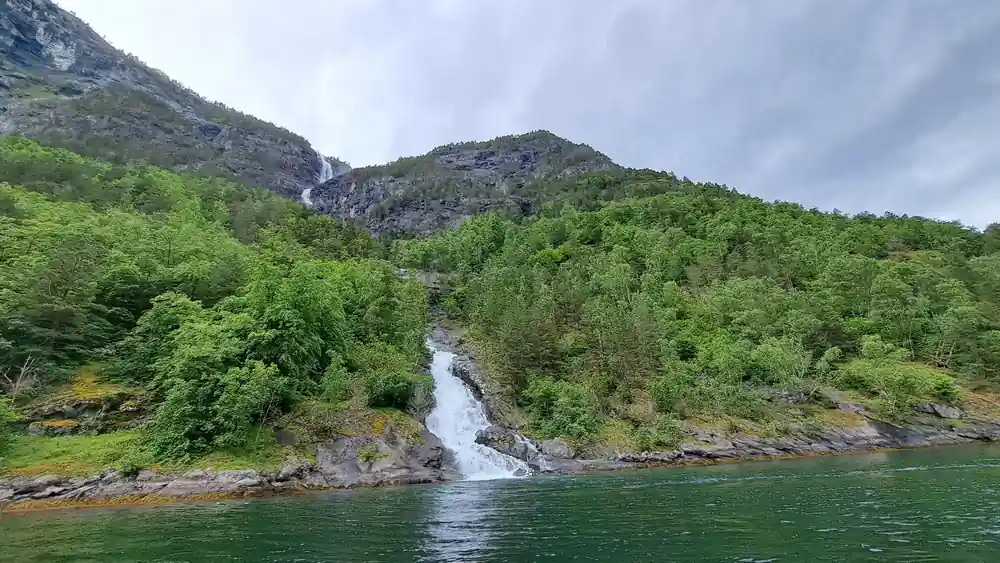 A waterfall running down a wooded slope into the fjord