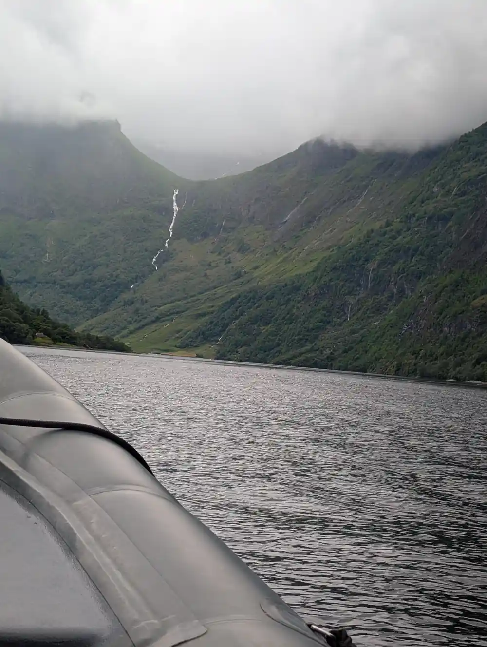 A wide grey fjord with a waterfall on the far wall